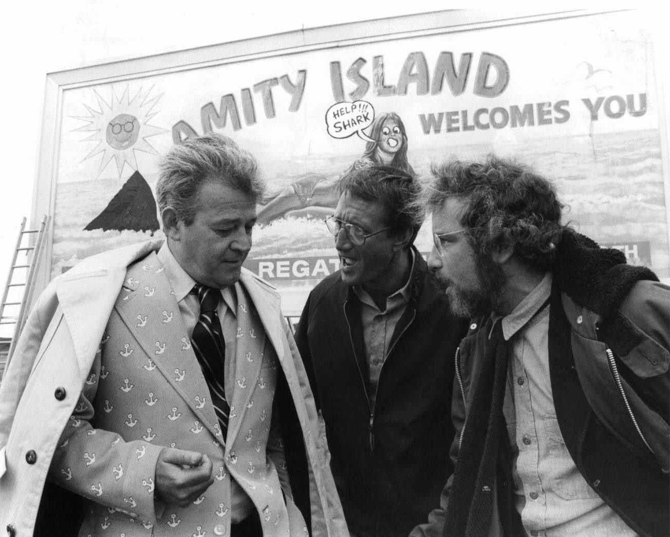 Murray Hamilton, Roy Scheider, and Richard Dreyfuss standing in front of defaced billboard in a scene from the film 'Jaws', 1975.