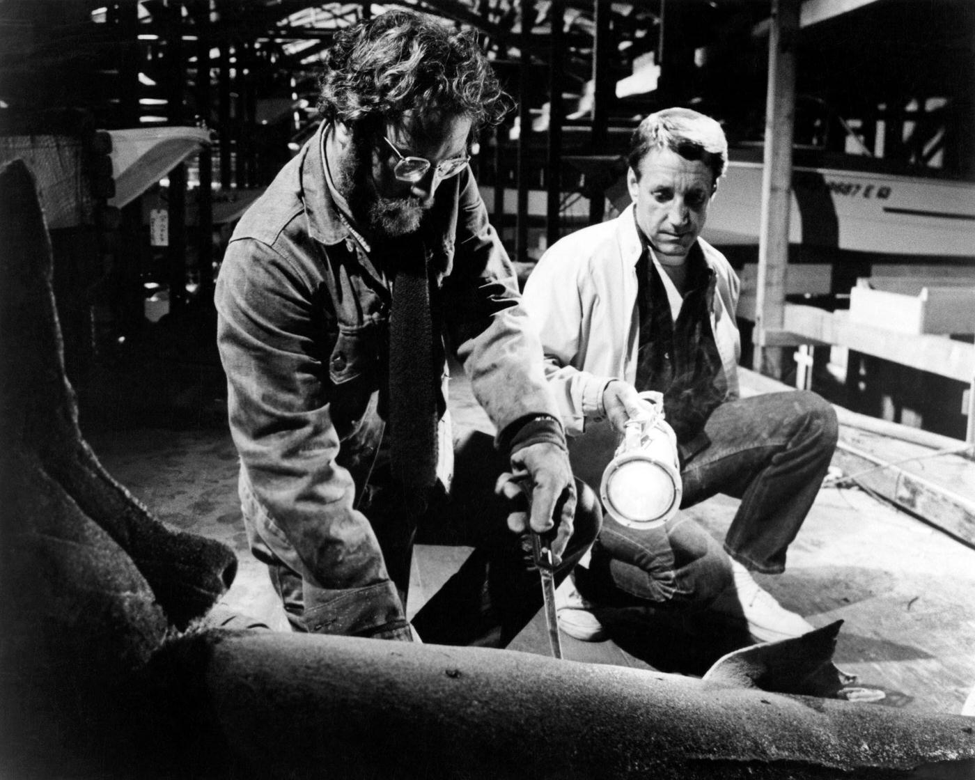 Police chief Martin Brody, played by Roy Scheider (1932 - 2008) holds a torch while marine biologist Matt Hooper (Richard Dreyfuss) cuts open the stomach of a recently caught tiger shark, in 'Jaws', 1975