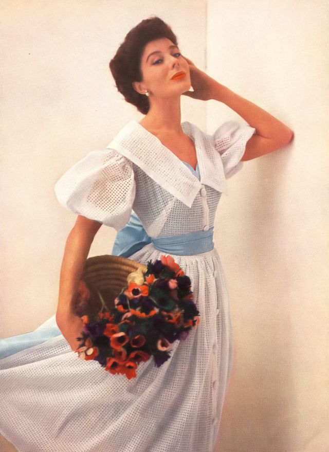 Bettina in dress with two lives; by day broderie Anglaise over sky-blue taffeta; at night the overdress is removed to reveal the lining as a short décolleté evening dress by Susan Small, 1952