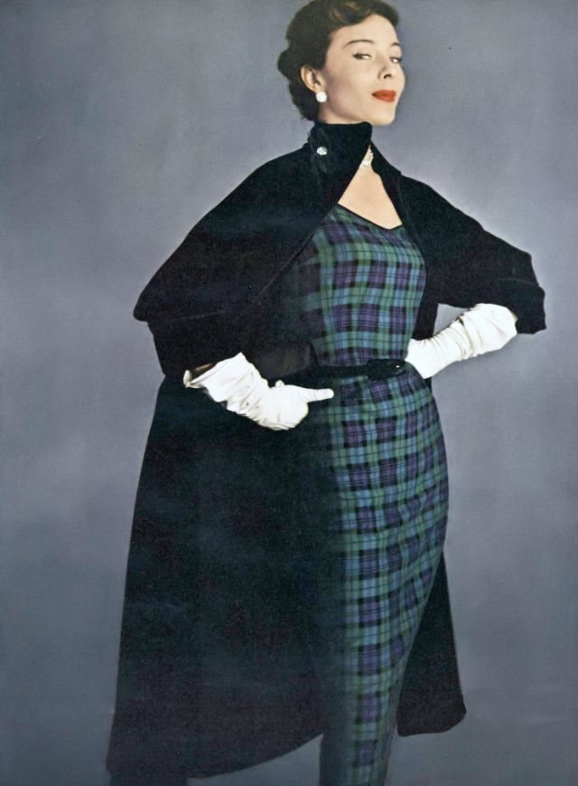 Bettina in plaid wool worsted sheath under a big black velveteen coat inter-lined and braid-bound, both by H. & D., earrings by Kramer, Vogue, August 15, 1950