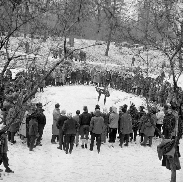 People standing around and watching a couple skating.