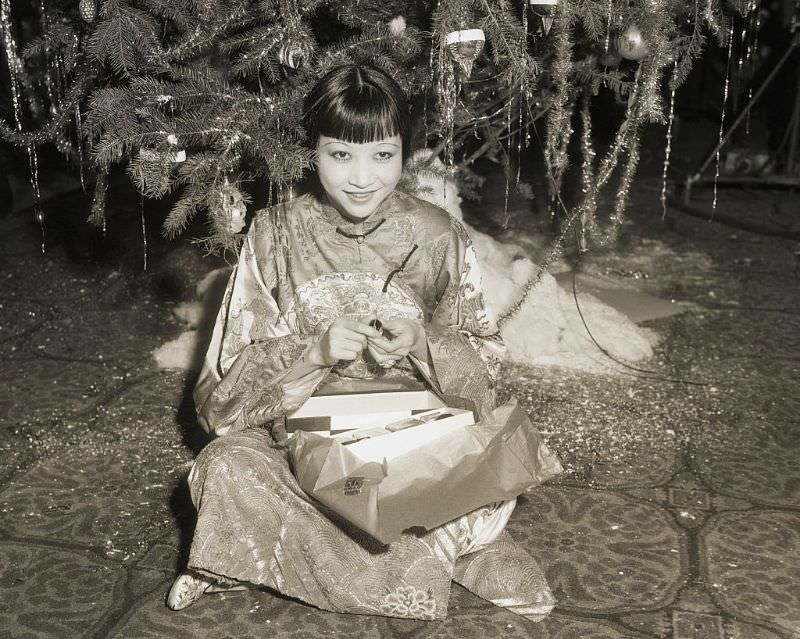 Anna May Wong opens present under the tree at a Christmas celebration for Hollywood stars at the Christy Hotel in 1932.