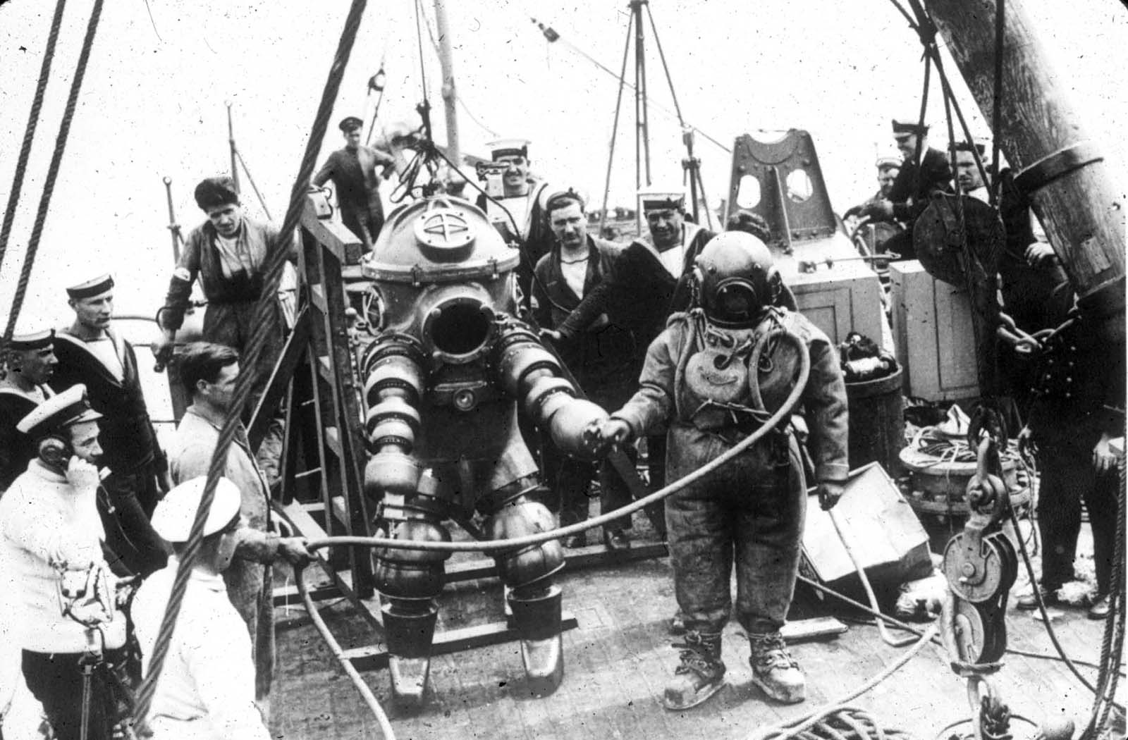 Two divers, one wearing the Tritonia ADS and the other standard diving dress, preparing to explore the wreck of the RMS Lusitania, 1935.