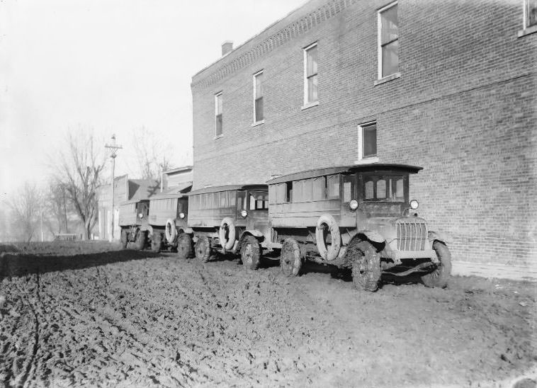 School Buses from the Strahan Consolidated School. Four Buses lined up waiting for students at the end of the day on a Very Muddy Street. The Buses have chains on all four tires, 1918