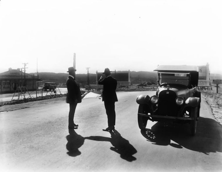 Two land developers standing in the middle of the road next to a Buick automobile parked near the end of Sloat Avenue and the Great Highway in San Francisco, California, 1921