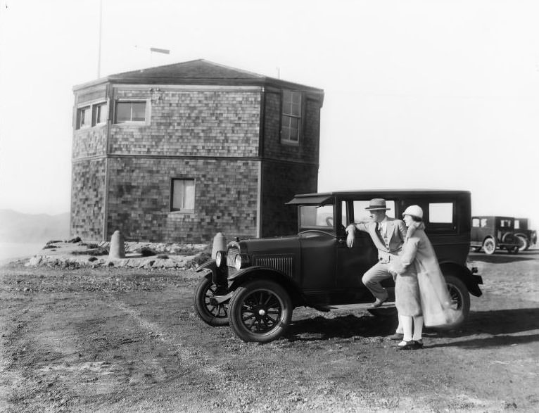 A 2-Door Sedan automobile pictured alongside the nearly completed historic "Octagon House" located at Lands End in San Francisco, California. Formally known as Point Lobos Marine Exchange Lookout Station, 1925