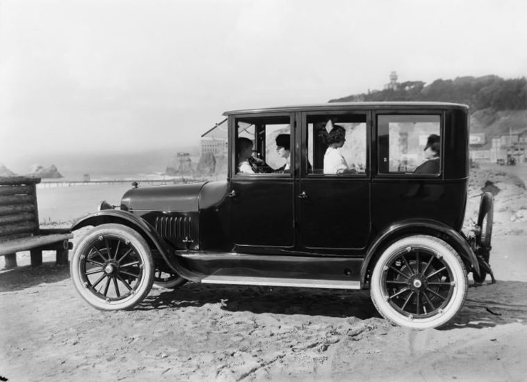 San Francisco's historic Cliff House and Seal Rocks as from beach level. An automobile loaded with a pair of ladies and two children pictured in the foreground, 1910s