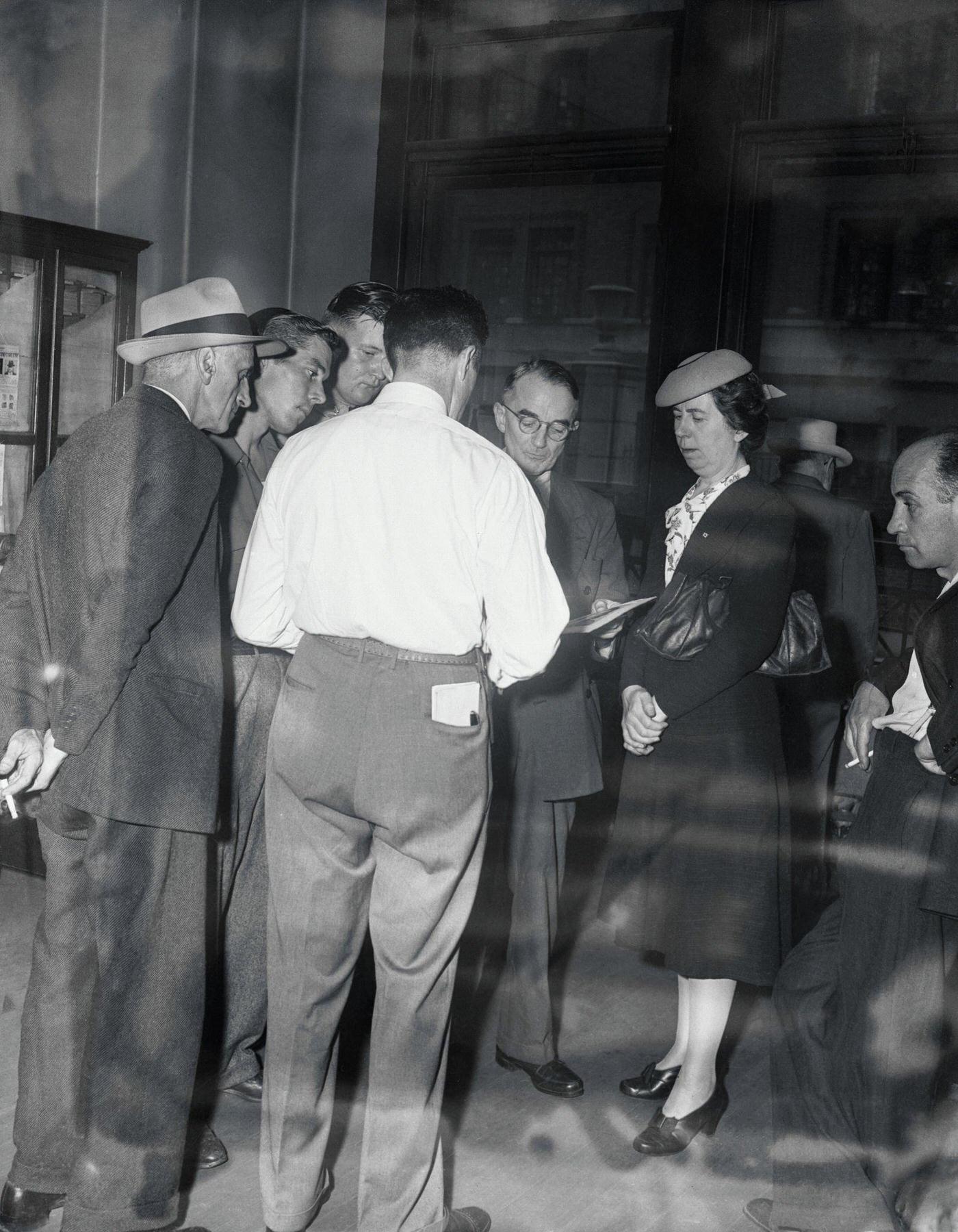 Grief-stricken relatives of Empire State plane crash dead talk with Detective Mullins (back to camera) at Bellevue Morgue. One man holds photo which was used to identify victim.