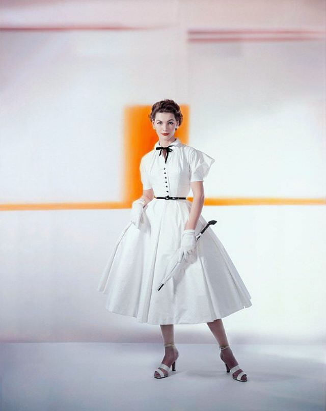 Georgia Hamilton wearing a white matelassé cotton with puffed cupid sleeves below the dropped shoulder, a black bowtie, jet buttons and a patent belt, by Caroline Schnurer, Glamour, 1952