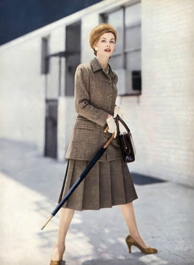 Georgia Hamilton in amber tweed suit with jacket that can be a coat, with pale-amber crêpe blouse, by Handmacher, beret by Emme, Gucci umbrella, Koret bag, Vogue, September 1, 1955