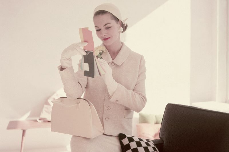 Georgia Hamilton sitting on arm of sofa wearing chamois yellow suit by Faye Wagner with felt helmet by Miss Ruth, linen-textured bag by Greta, 1955