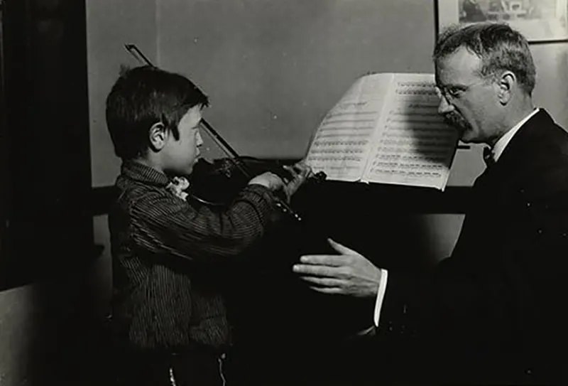 A young refugee with musical talent receives instruction in Hull House music studio, 1910.