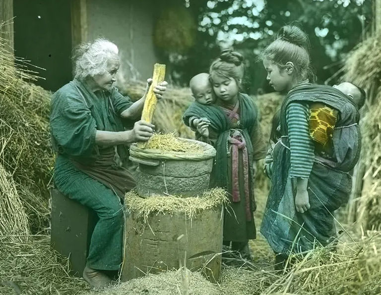 Old woman with raised grinding stone; two little girls carrying babies on their backs looking on.