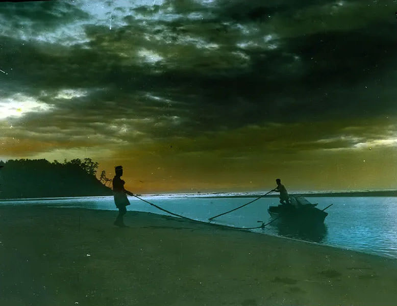 Two men landing boat on beach.