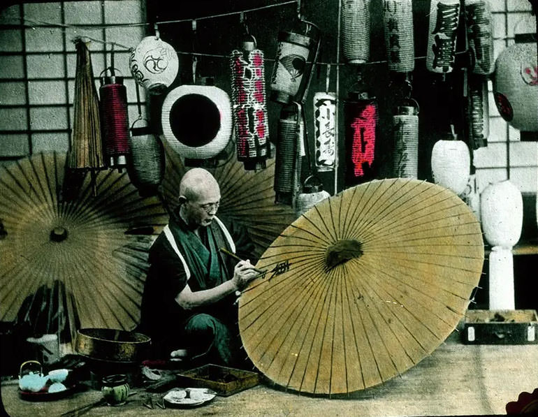 Man painting parasols; painted lanterns in background.