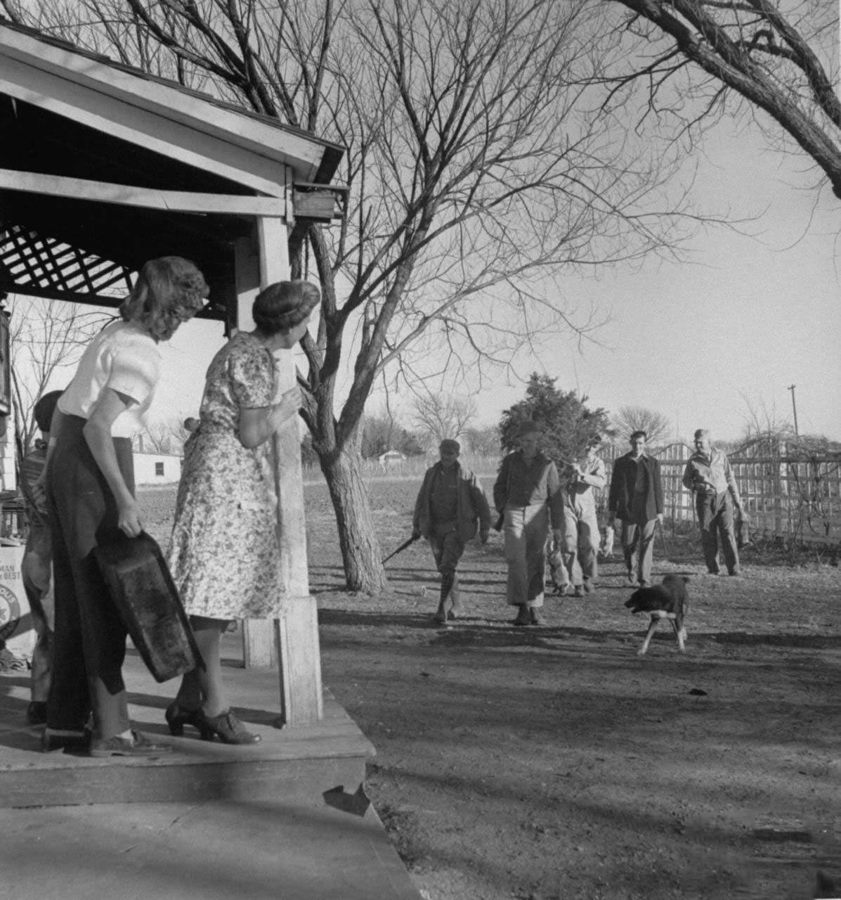 Mrs. James Ferdinand Irwin (L) standing on porch watching the men in her family, most recently returned fr. service in WWII, carrying home freshly shot rabbits and a cedar tree for Christmas family reunion.