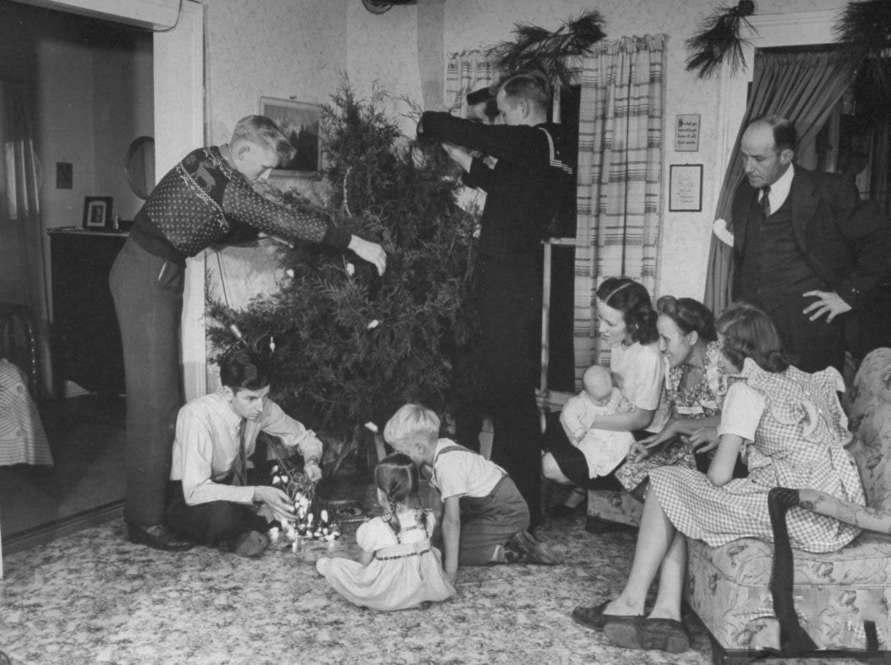 Members of farmer James Ferdinand Irwin's family trimming native cedar Christmas tree in living room during family reunion and early Christmas celebration marking the return of Irwin's sons and sons-in-law from service in WWII.