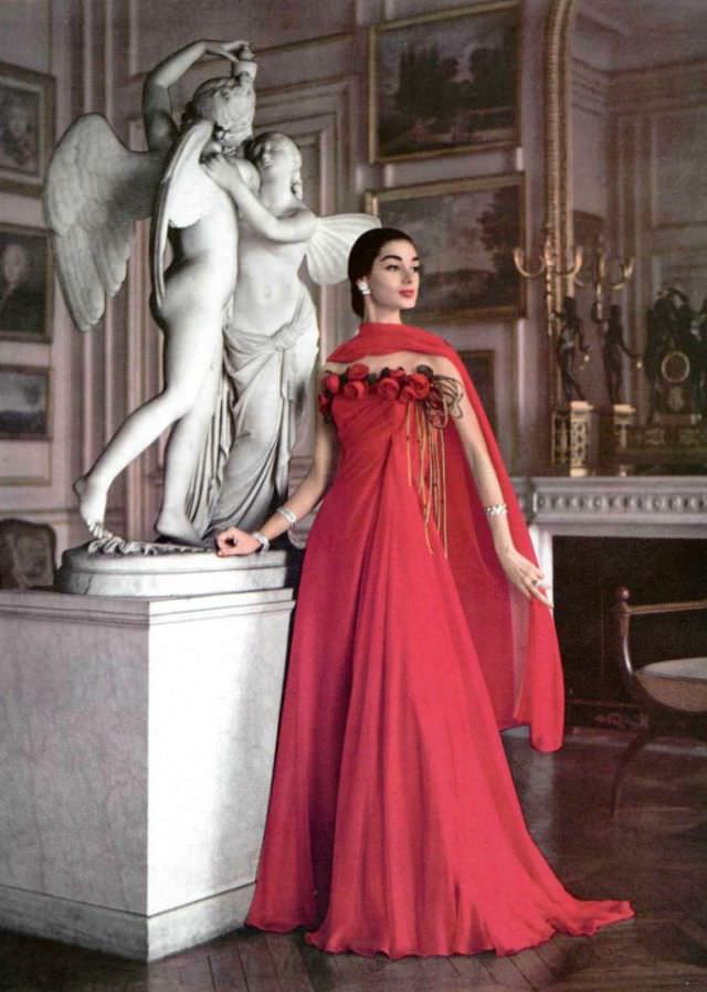 Jacky Mazel in fiery red chiffon gown, a row of roses borders the draped bodice, by Grès, jewelry by Boucheron, Paris, 1956