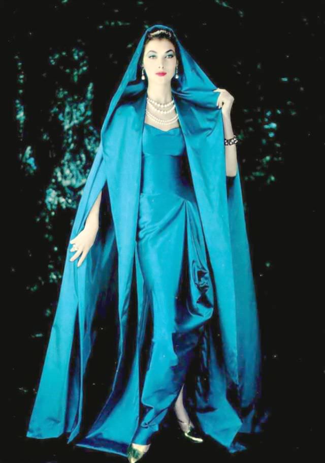 Rose Marie in gorgeous blue draped satin gown gathered at the hip and split at the ankles worn under a hooded cloak of same material by Grès, 1957