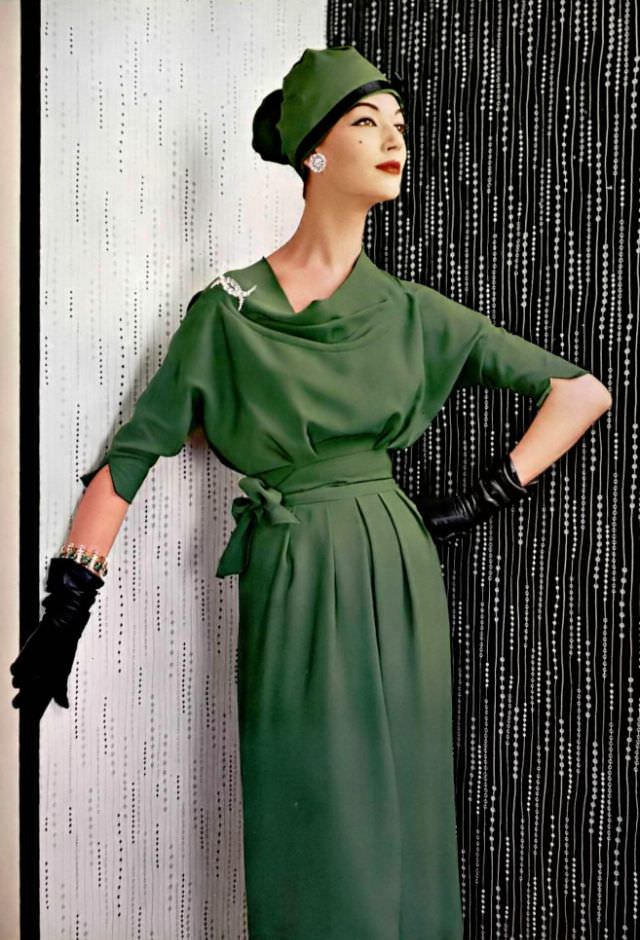 Simone d'Aillencourt in green crêpe dress, the supple bodice with cowl neck ends in scalloped sleeves, belt of the same material is tied in knot at the side, by Grès, jewelry by Roger Scémama, 1957