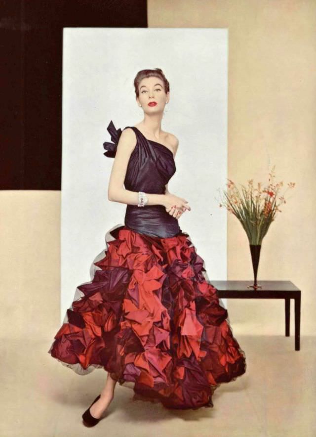 Model in evening gown of extraordinary work in taffeta, the elongated bodice has one shoulder knotted in back, skirt is made of shells in several tones covered with fine net of black tulle by Grès, 1952