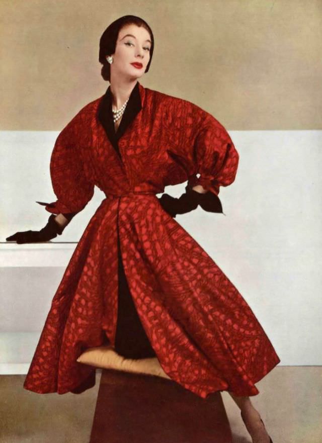 Model in red printed satin evening coat with full balloon sleeves, the collar and cuffs lined in black silk, two-button closure at the waist, 1952