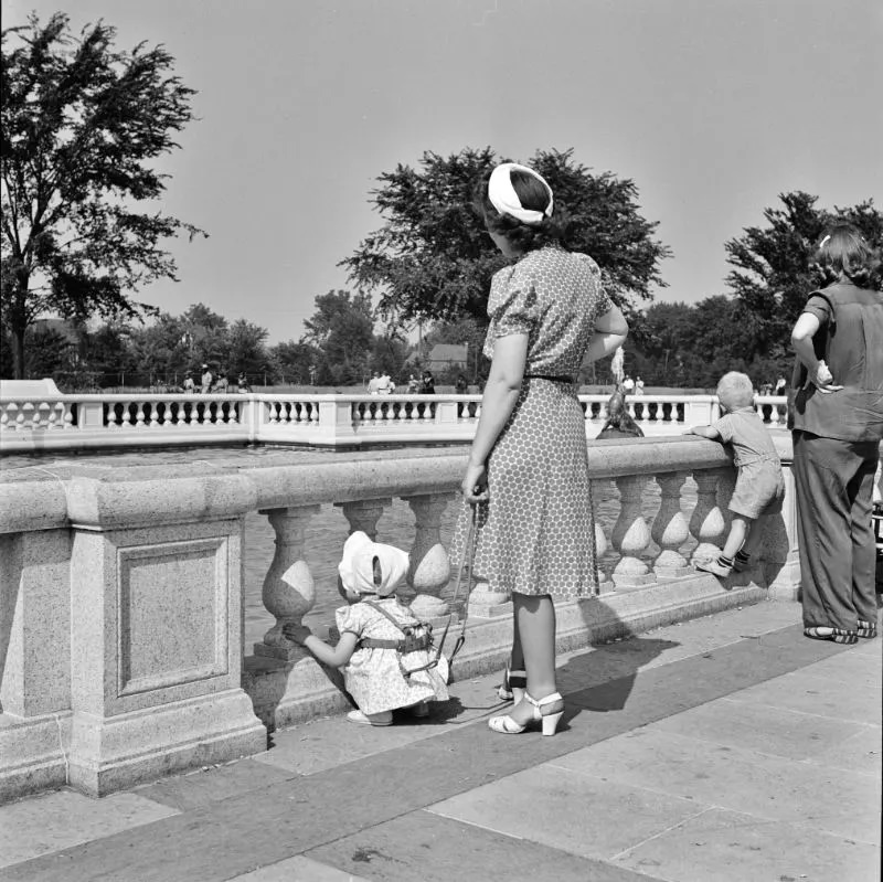 Woman adjusting a harness strap to prevent child from getting lost in zoological park, Detroit, Michigan, July 1942.