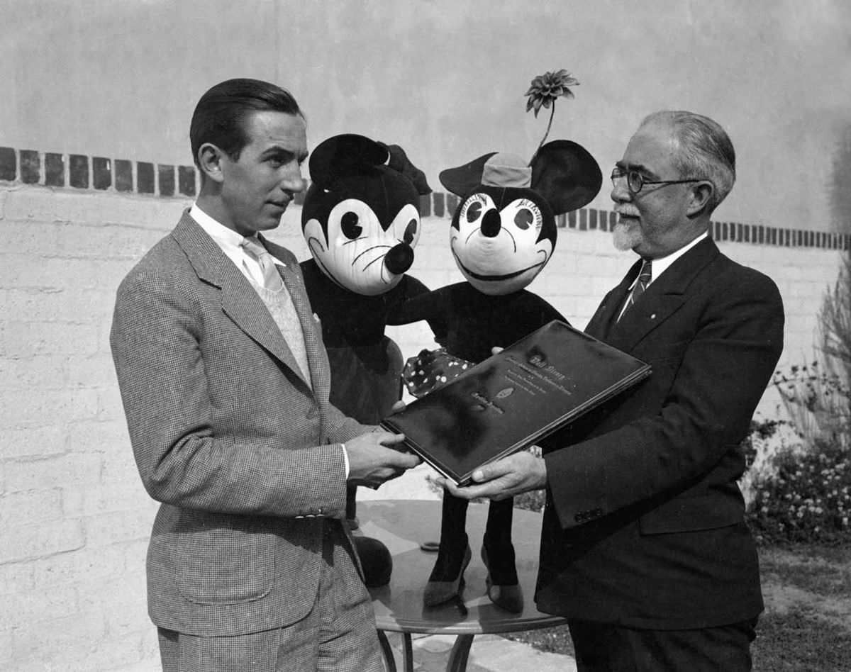 Walt Disney presented with a diploma of commendation from the National Academy of Fine Arts of Buenos Aires, Argentina. Mickey and Minnie look on, 1933.