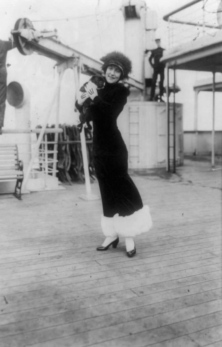 Annette Kellerman, full-length portrait, standing on deck of ship, facing front, holding a black pug (dog)