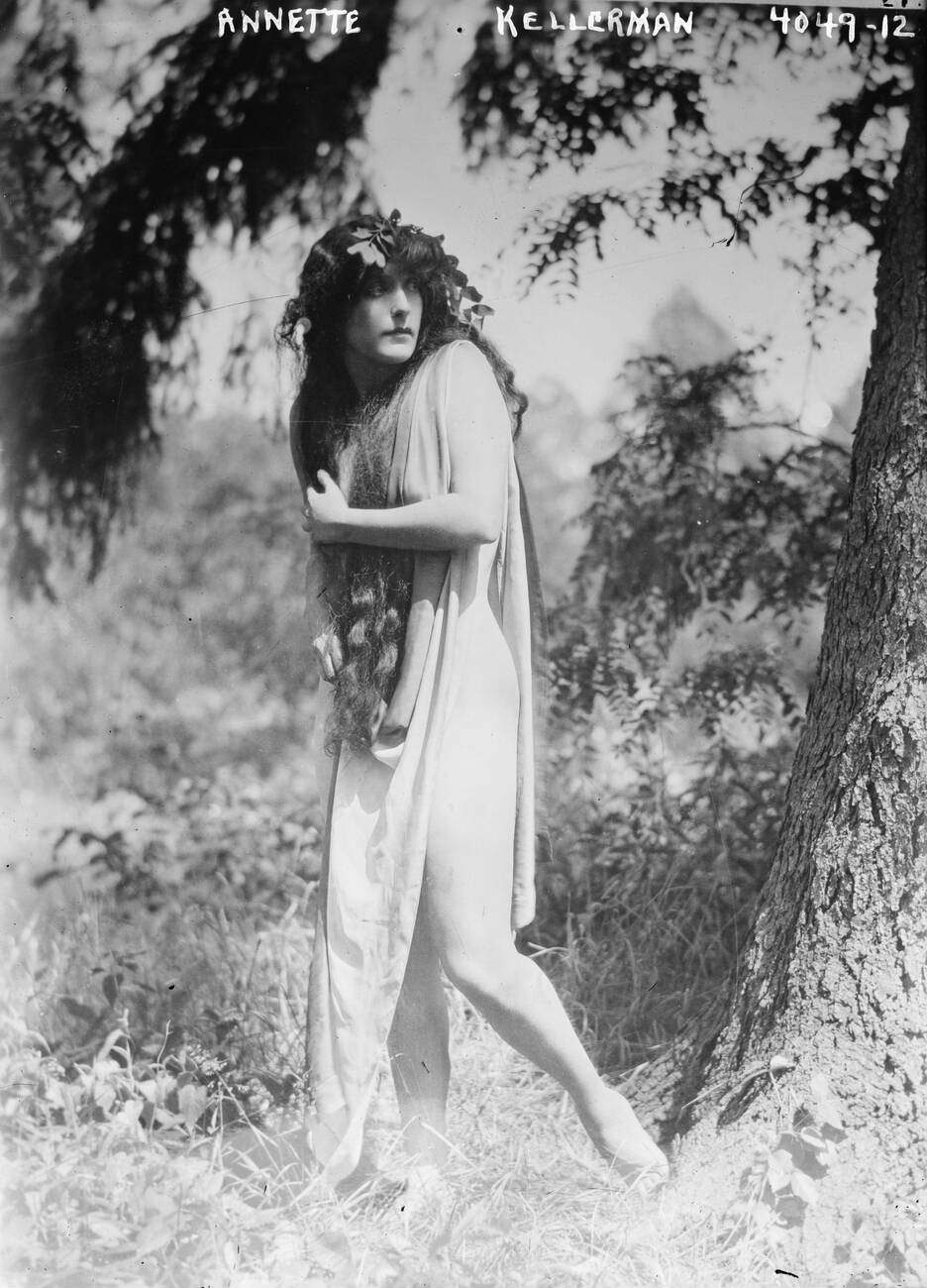 Annette Kellerman standing in neo-Classical robe, looking backwards.