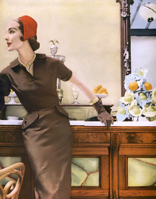 Cherry Nelms in taupe silk twill sheath by Mollie Parnis, red brushed velours cap by John Frederics, gold and diamond necklace and bracelet by Van Cleef & Arpels, Vogue, July 1953