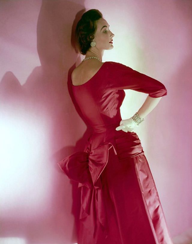 Evelyn Tripp in a red silk twill dress with a bustle-bow by Mollie Parnis, rhinestone jewellery by Bogoff, Vogue, November 15, 1953