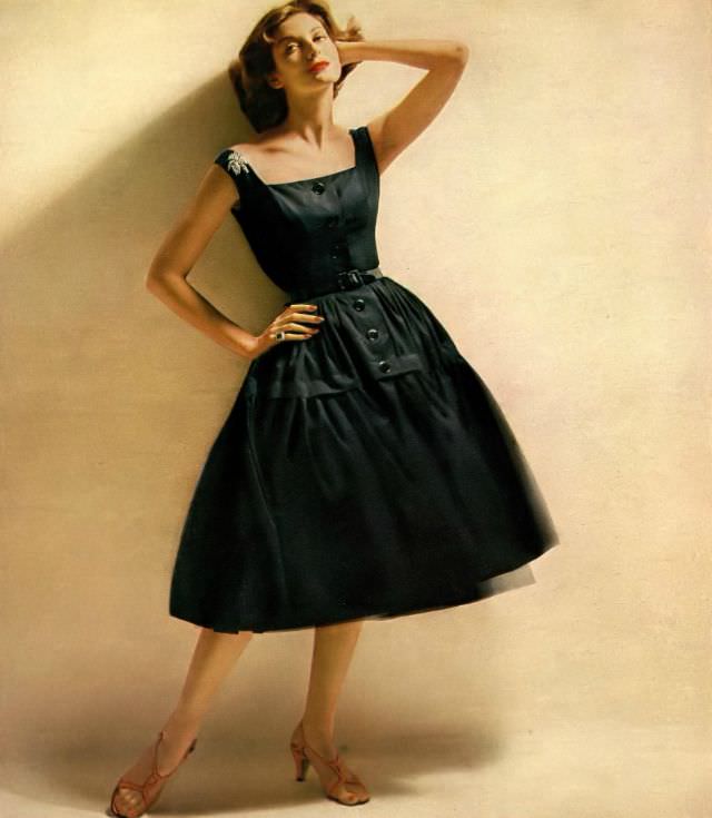 Carmen Dell' Orefice in very pretty dress of black piqué swirling out from a camisole bodice by Mollie Parnis, diamond brooch and ring by Harry Winston, 1956