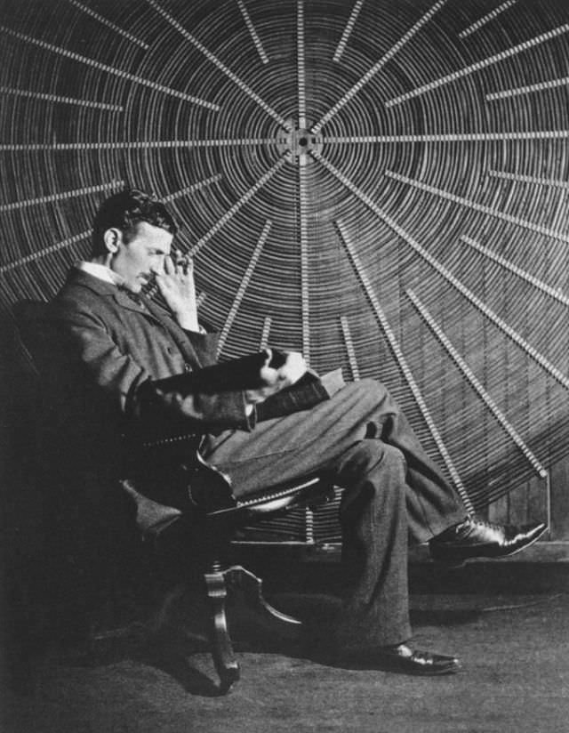 Nikola Tesla, with Roger Boskovich’s book, “Theoria Philosophiae Naturalis,” in front of the spiral coil of his high-frequency transformer at East Houston St. 46, New York.