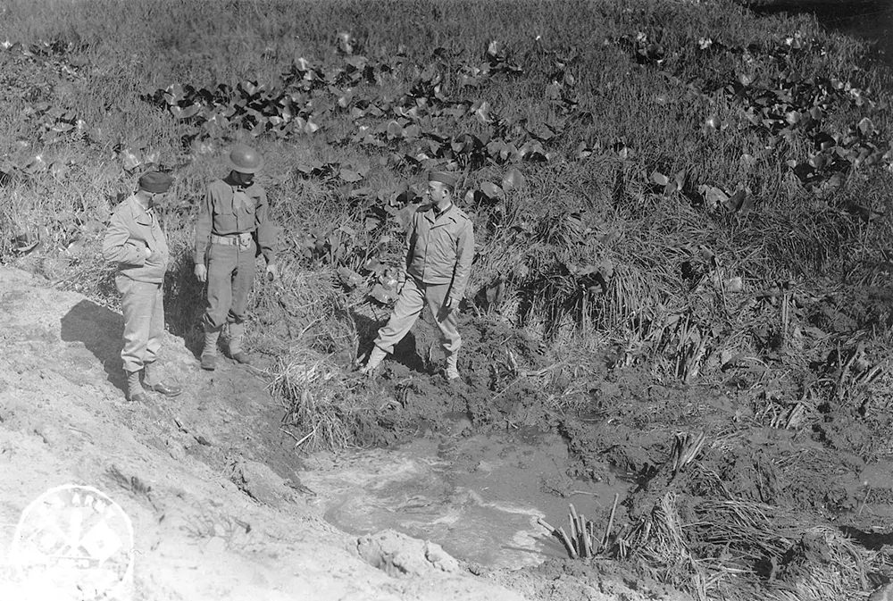 American servicemen inspecting a shell crater after the Japanese attack on Fort Stevens.