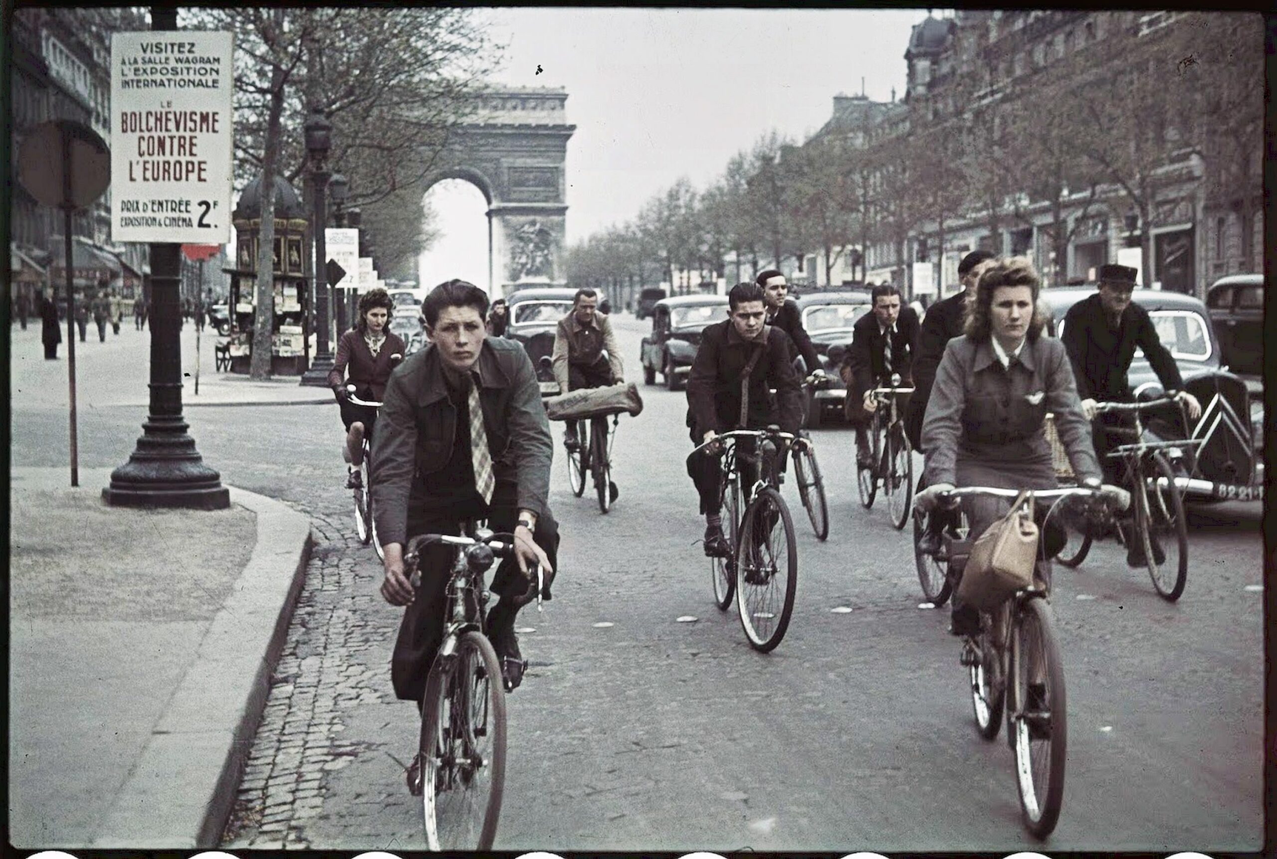 Parisians cycle past a poster for Nazi-sponsored Europe Against Bolshevism exhibition.