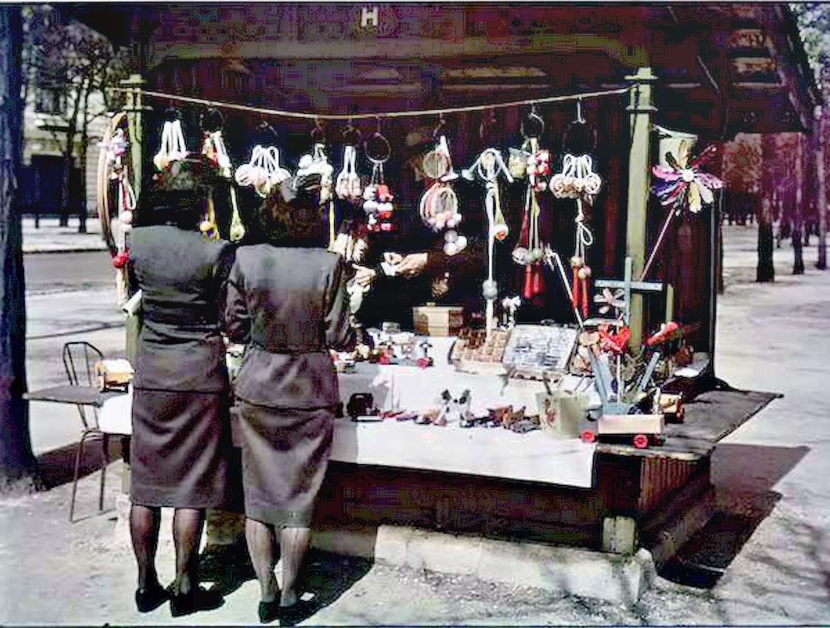 Two women in military-style uniforms shop at a stall selling toys.