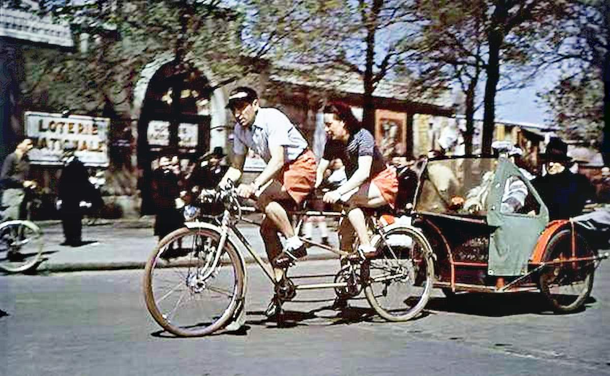A wealthy-looking man and woman ride in a cart pulled by two slim Parisians on a tandem bicycle.