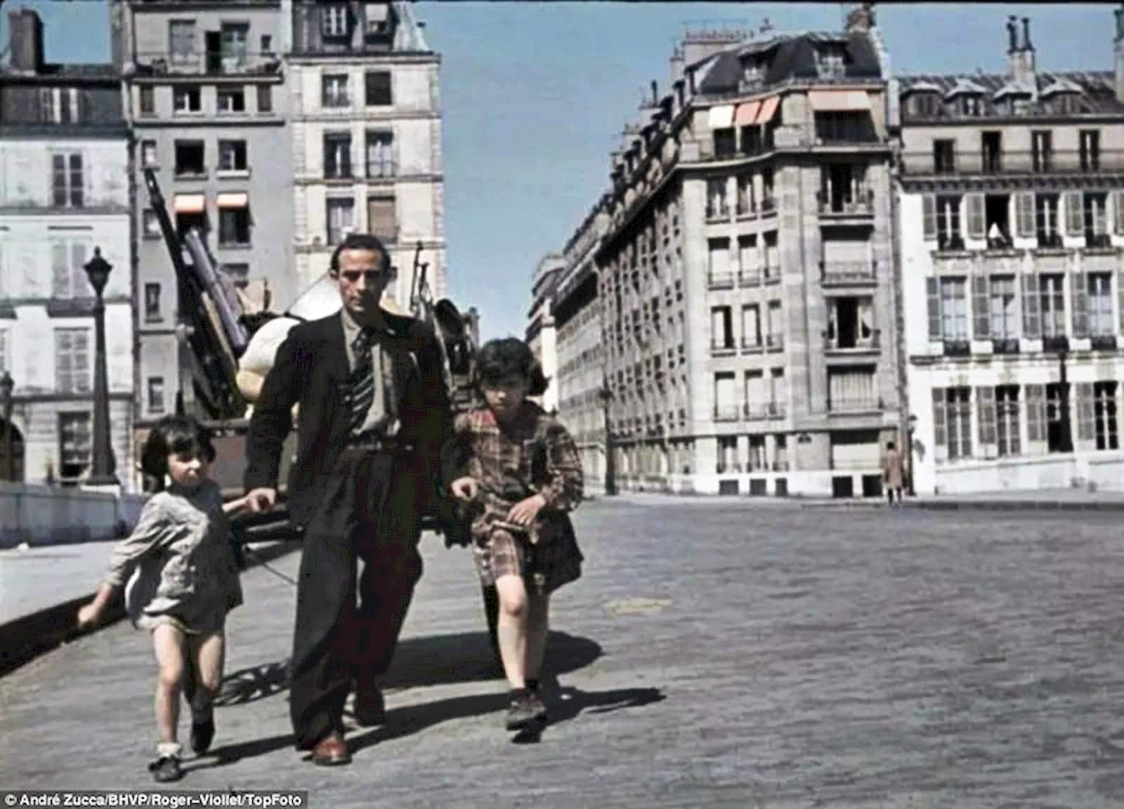 A harried-looking man with two scruffily dressed girls drags a cart through the streets of Paris.