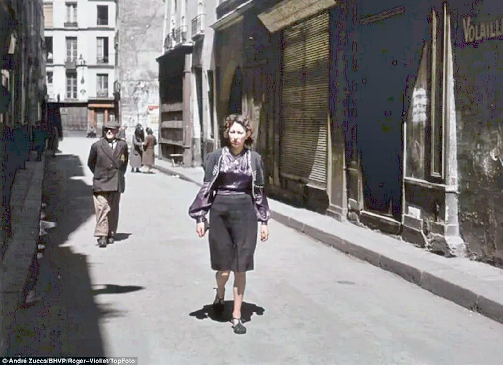 A woman walks a Parisian backstreet, in front of an older gentleman who is marked with the Star of David insignia that Jews were forced to wear.