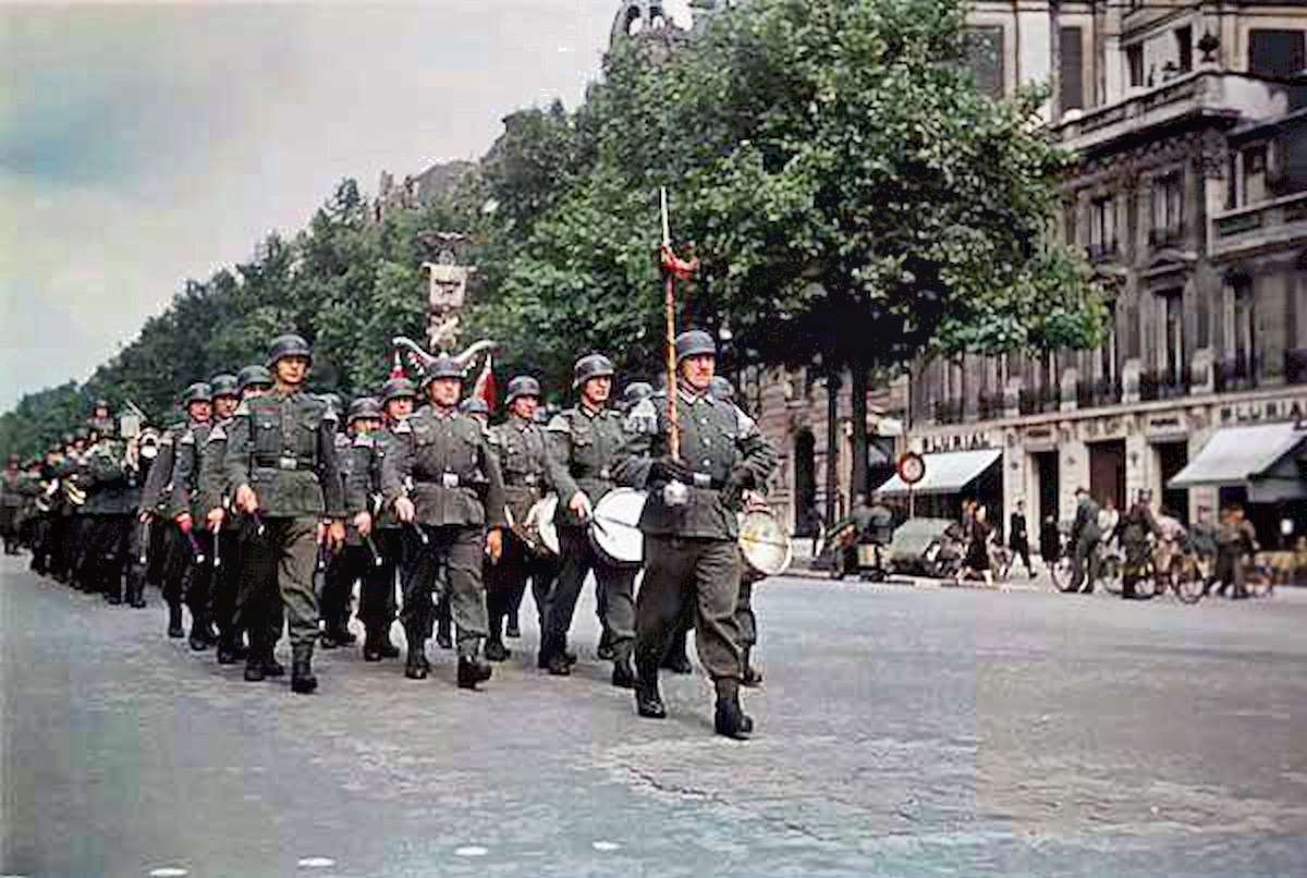 Stern-looking soldiers from the Wehrmacht march down one of the city’s broad boulevards.