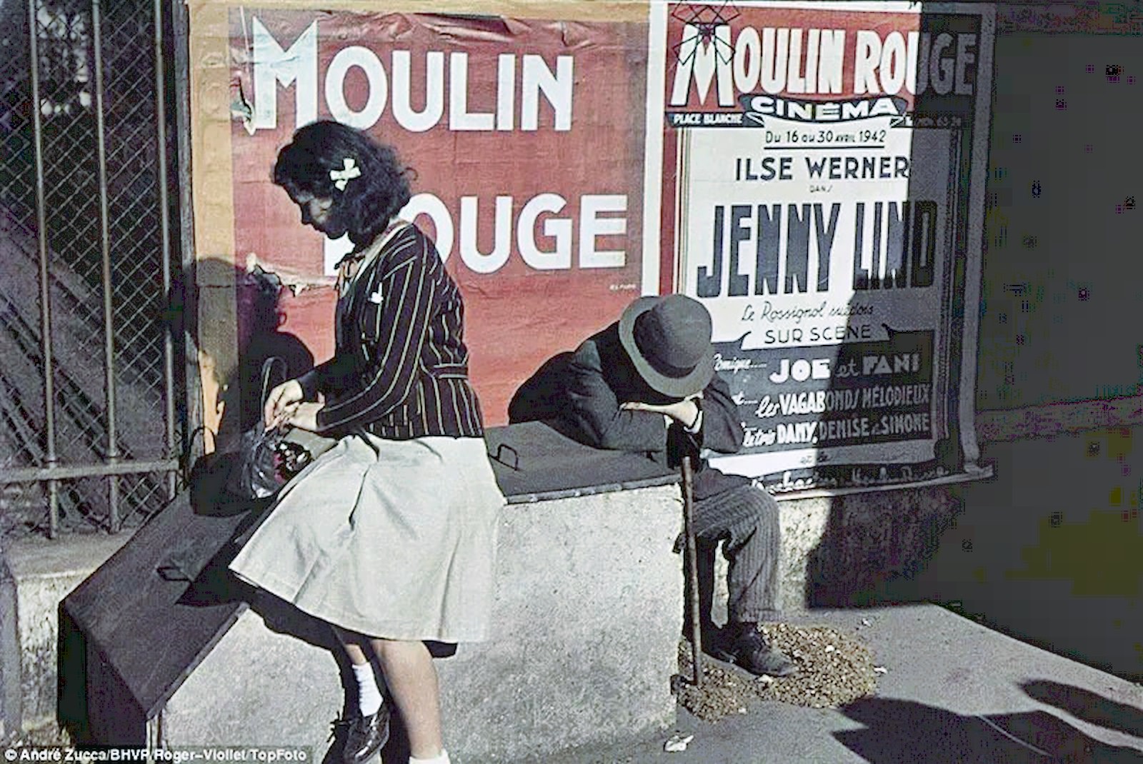 A young woman checks her handbag while a man sits slumped over a walking stick in front of posters for the City’s famous Moulin Rouge cabaret.