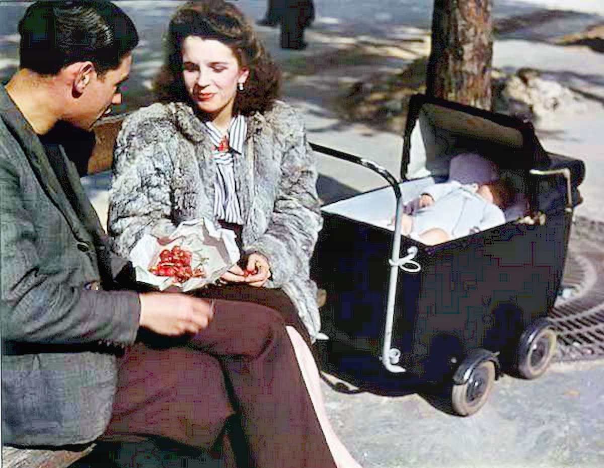 A young family, including a man of usual conscription age, sit in the sunshine eating cherries.