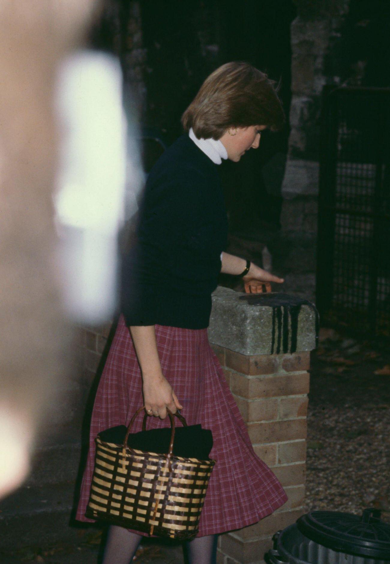 Lady Diana wearing a dark sweater with a deep red plaid skirt, and carrying a brown handbag, leaves the Young England kindergarten in Pimlico, London, England, October 1980.