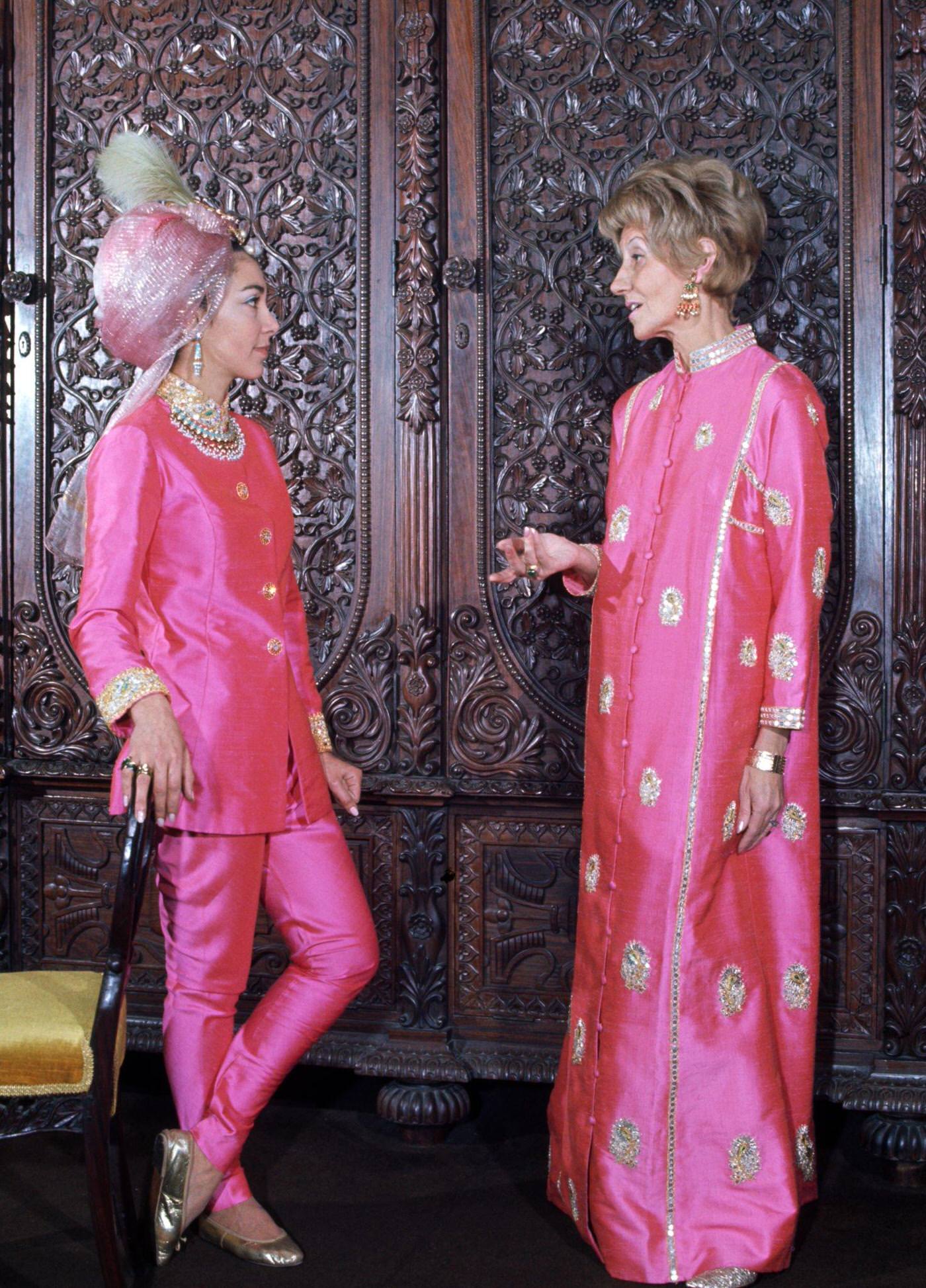 Two women in a hippie fashion boutique, one wears a two piece trouser suit in pink silk with a pink turban head dress and gold ballet shoes, the other wears a full length pink silk Kaftan with gold embroidery, London, 1966