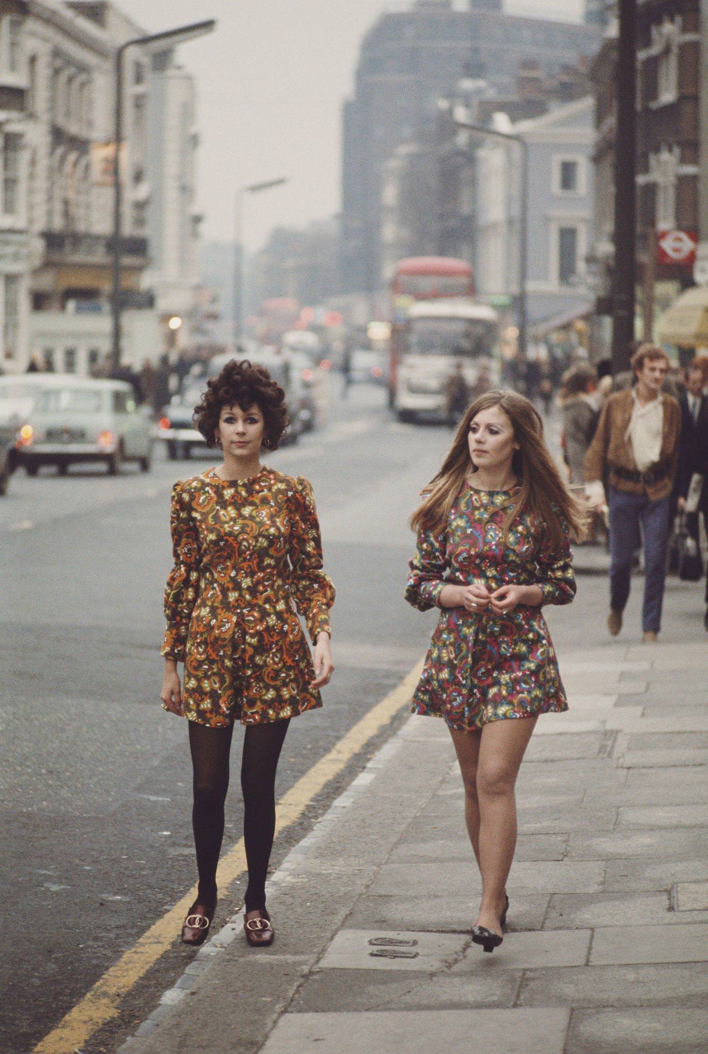 Two young girls dressed in long sleeved floral print mini dresses walk along the Kings Road in Chelsea, London in November 1967.