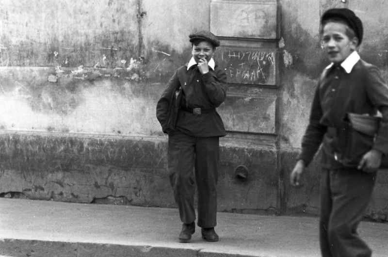 Two boys in uniform smiling on the sidewalk.