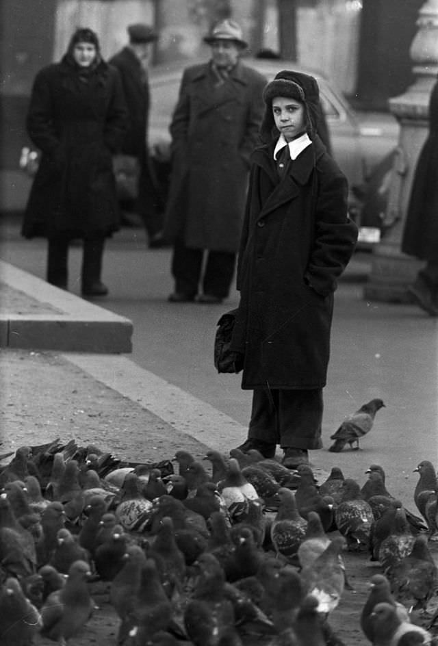 A young boy dressed in cold clothes and carrying his satchel.