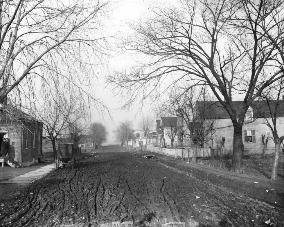 Unpaved road that is muddy, many ruts from carriage wheels are visible, 1900.