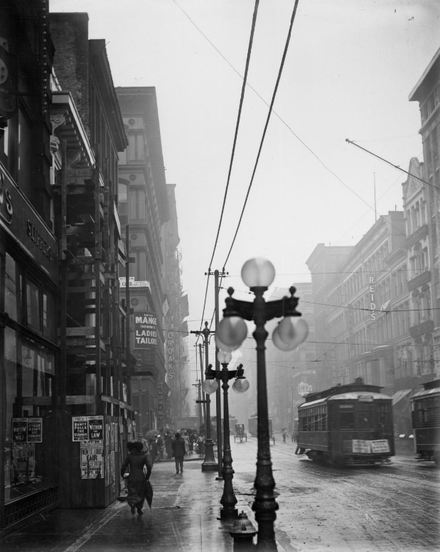 Rainy city street with street lamps visible in the foreground, 1900
